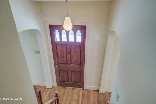 entryway with baseboards, arched walkways, and wood finished floors