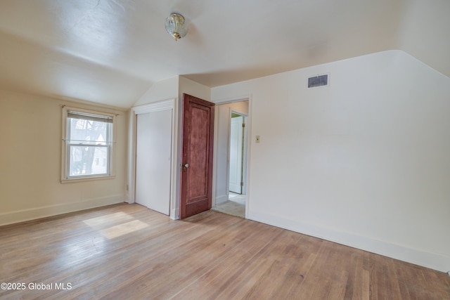 empty room featuring visible vents, light wood-type flooring, baseboards, and vaulted ceiling