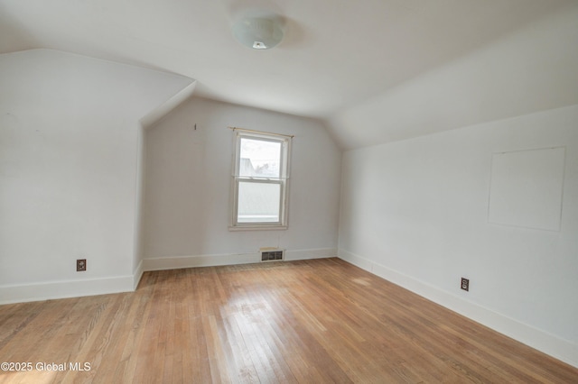 additional living space with visible vents, baseboards, lofted ceiling, and light wood-style floors