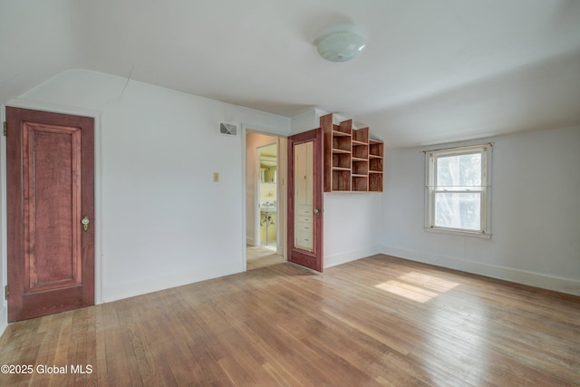 interior space featuring visible vents, baseboards, light wood-style flooring, and vaulted ceiling