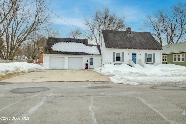 cape cod house with a garage, driveway, and a chimney