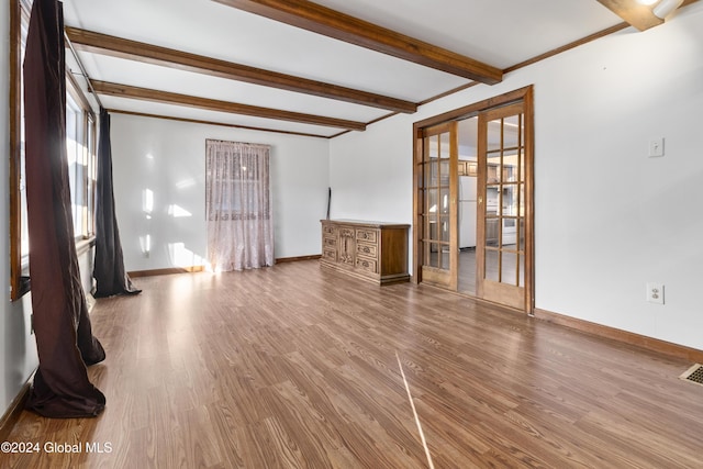 spare room with visible vents, beamed ceiling, baseboards, and wood finished floors