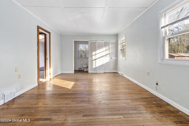 empty room featuring baseboards, wood-type flooring, visible vents, and crown molding