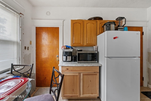 kitchen featuring radiator heating unit, stainless steel microwave, and freestanding refrigerator