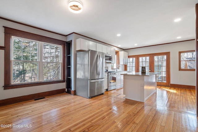 kitchen with visible vents, light wood-style floors, appliances with stainless steel finishes, white cabinetry, and crown molding