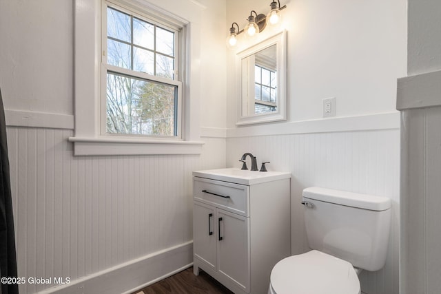 bathroom with vanity, toilet, wood finished floors, and a wainscoted wall