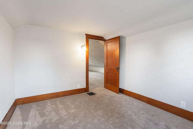 spare room with visible vents, baseboards, carpet, and vaulted ceiling