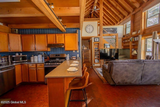 kitchen with wooden ceiling, under cabinet range hood, stainless steel appliances, a kitchen breakfast bar, and open floor plan