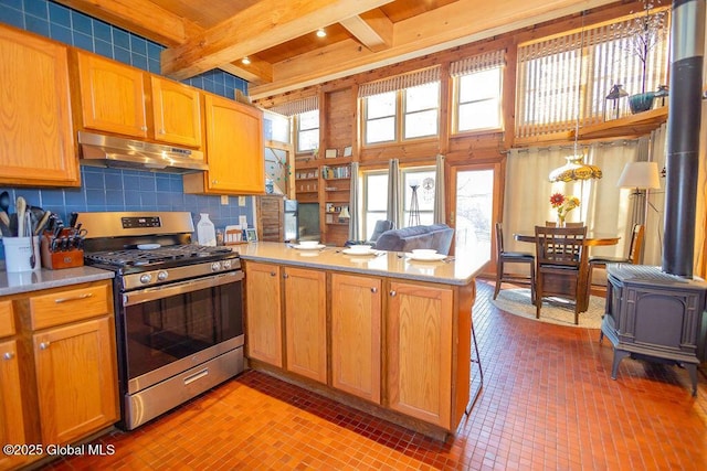 kitchen with gas range, beamed ceiling, a peninsula, a wood stove, and under cabinet range hood