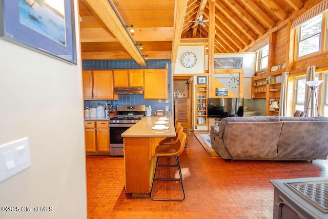 kitchen featuring beam ceiling, tasteful backsplash, wood ceiling, under cabinet range hood, and stainless steel gas range oven