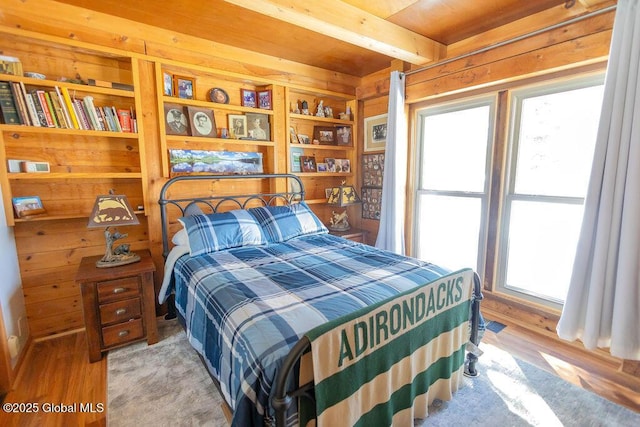 bedroom with wood walls, wood finished floors, and beamed ceiling