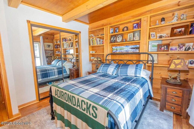 bedroom featuring beam ceiling, baseboards, and wood finished floors