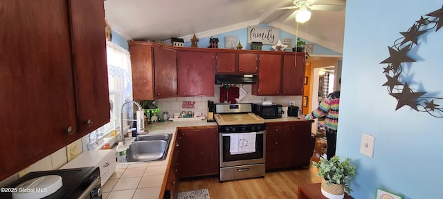 kitchen with tile countertops, vaulted ceiling with beams, under cabinet range hood, a sink, and stainless steel range with gas stovetop