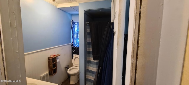 bathroom featuring a shower with shower curtain, a wainscoted wall, ornamental molding, and toilet