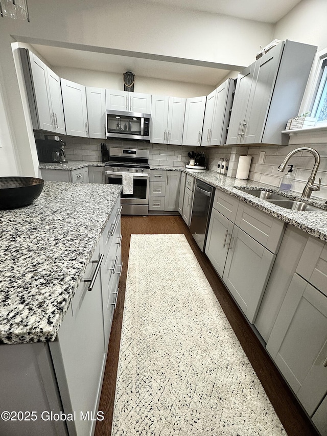 kitchen with appliances with stainless steel finishes, a sink, light stone counters, and decorative backsplash