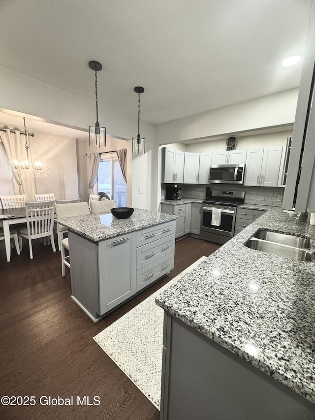 kitchen with a kitchen island, a sink, appliances with stainless steel finishes, backsplash, and dark wood finished floors