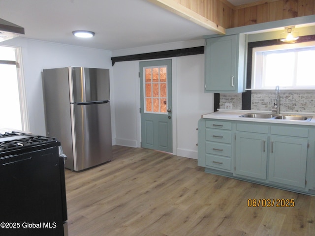 kitchen featuring freestanding refrigerator, a sink, black range with gas stovetop, light wood-type flooring, and backsplash