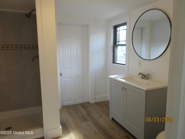 bathroom featuring tiled shower, wood finished floors, and vanity