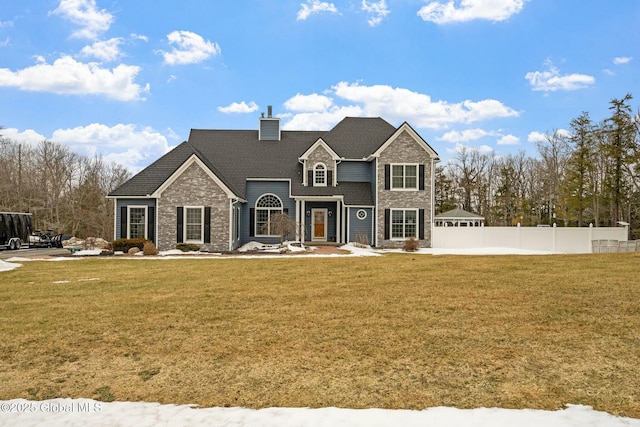 view of front of home with stone siding, a chimney, a front lawn, and fence