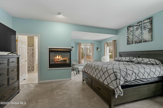 bedroom with a glass covered fireplace, baseboards, ensuite bathroom, and light carpet