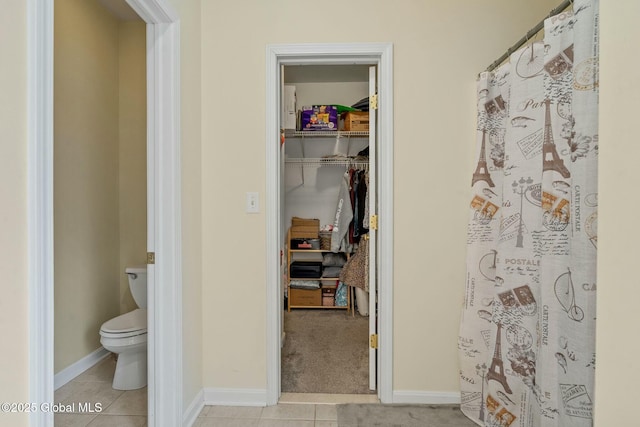 bathroom featuring tile patterned floors, toilet, curtained shower, baseboards, and a spacious closet