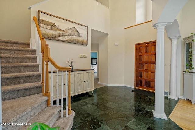 foyer featuring stairway, baseboards, a high ceiling, and ornate columns