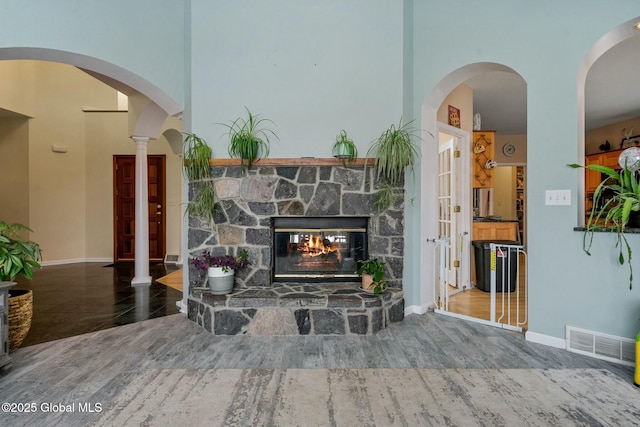 interior space featuring visible vents, baseboards, a stone fireplace, a towering ceiling, and wood finished floors