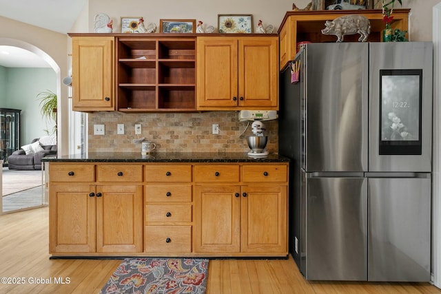 kitchen with light wood-style floors, dark stone countertops, arched walkways, and smart refrigerator