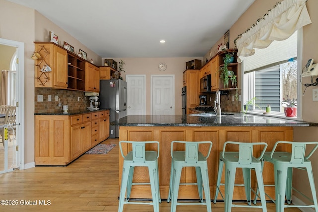 kitchen with open shelves, light wood-style flooring, a peninsula, a sink, and black appliances