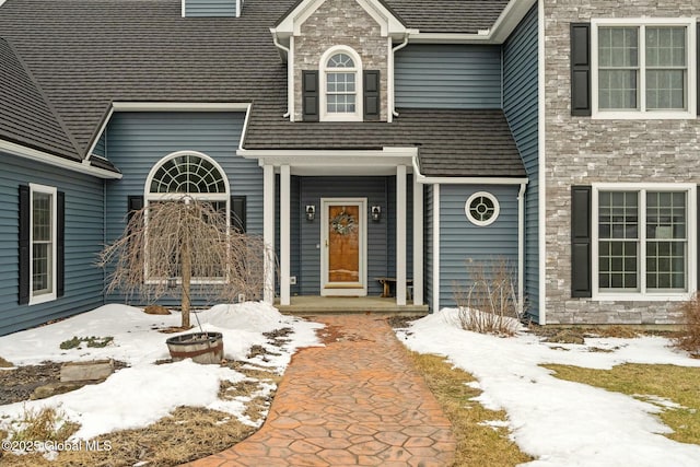 snow covered property entrance featuring stone siding