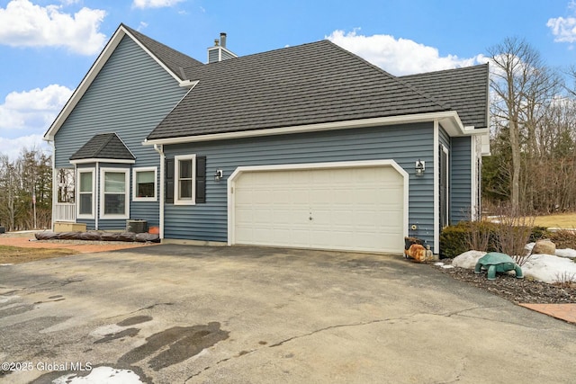 exterior space with roof with shingles, an attached garage, driveway, and a chimney