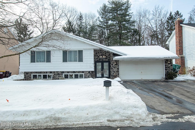 split level home with a garage, stone siding, driveway, and french doors