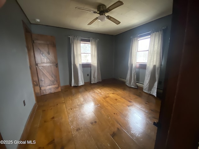 unfurnished bedroom with wood-type flooring, multiple windows, baseboards, and a ceiling fan