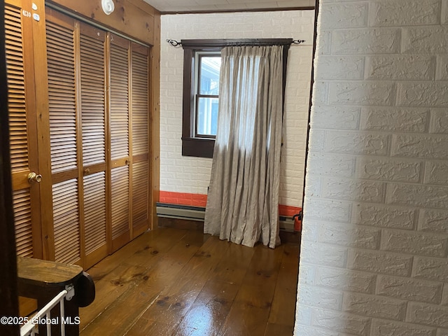 unfurnished bedroom with brick wall, a closet, a baseboard radiator, and hardwood / wood-style flooring