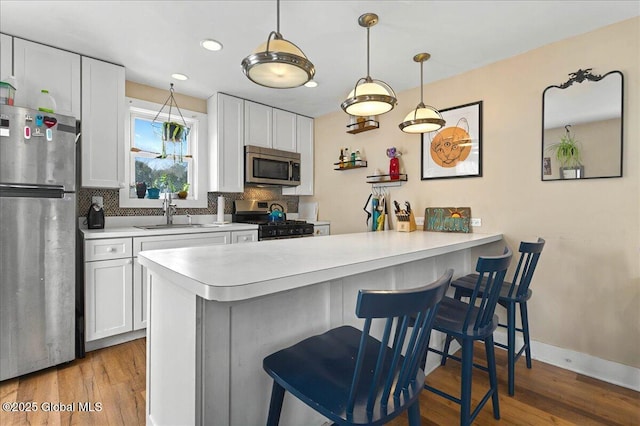 kitchen with stainless steel appliances, tasteful backsplash, light countertops, a sink, and a peninsula