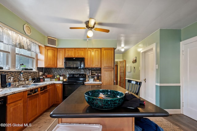 kitchen featuring tasteful backsplash, a wainscoted wall, a center island, black appliances, and a sink