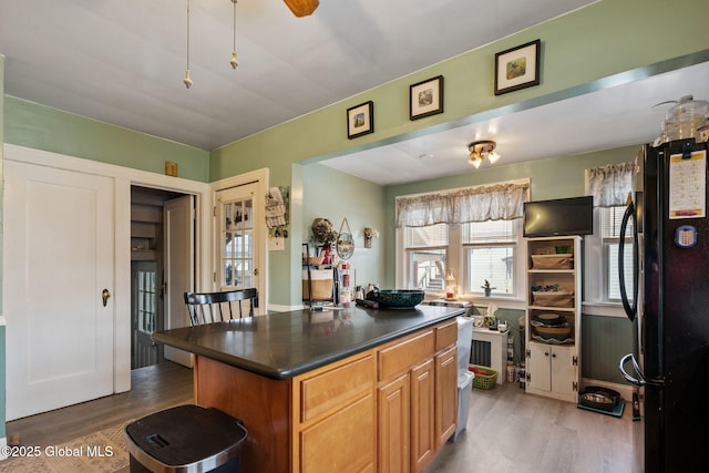 kitchen featuring light wood finished floors, dark countertops, a kitchen island, and freestanding refrigerator