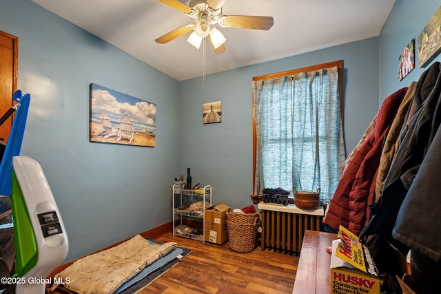 interior space with a ceiling fan, radiator heating unit, and wood finished floors