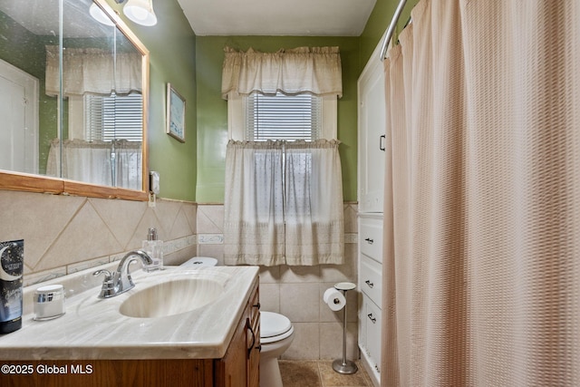 bathroom featuring toilet, a shower with shower curtain, vanity, tile walls, and wainscoting