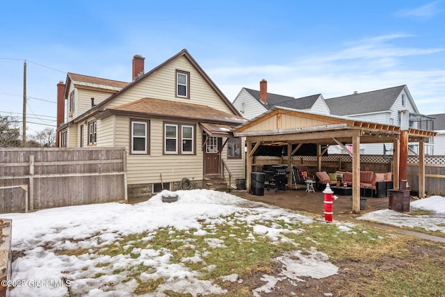 snow covered back of property featuring entry steps, roof with shingles, a chimney, and fence