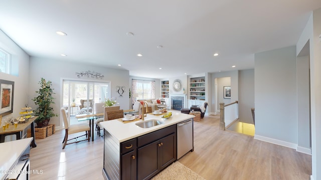 kitchen featuring light wood finished floors, light countertops, open floor plan, a sink, and dishwasher