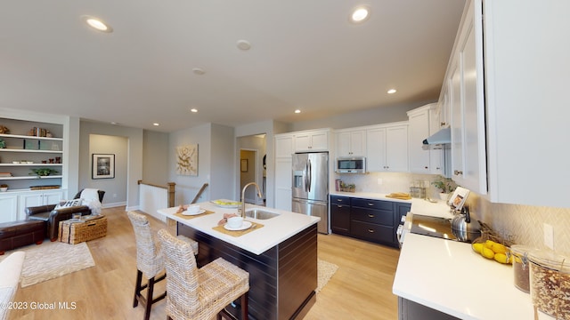 kitchen with light wood finished floors, appliances with stainless steel finishes, a sink, under cabinet range hood, and a kitchen bar