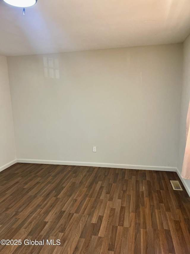 unfurnished room featuring dark wood-style floors, visible vents, and baseboards