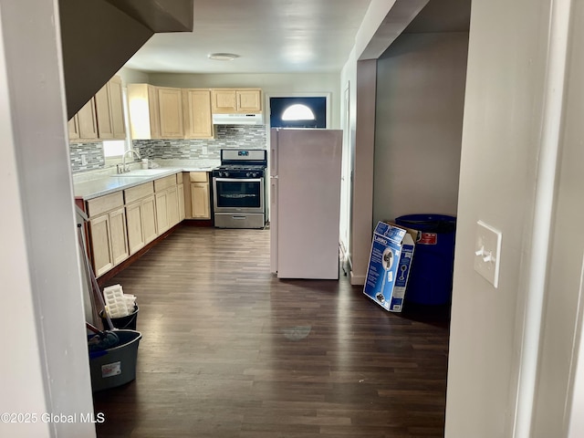 kitchen with under cabinet range hood, a sink, stainless steel gas range, freestanding refrigerator, and light brown cabinetry