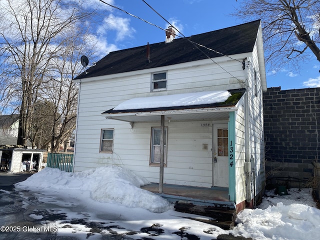 snow covered back of property featuring covered porch, a chimney, and fence