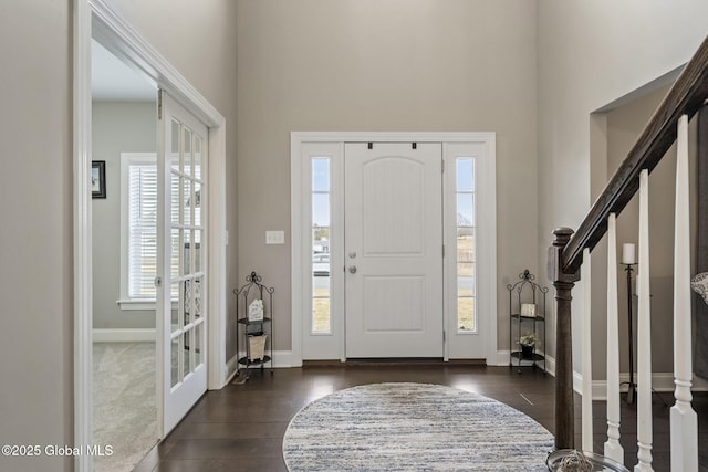 entryway featuring a towering ceiling, baseboards, dark wood finished floors, and stairs