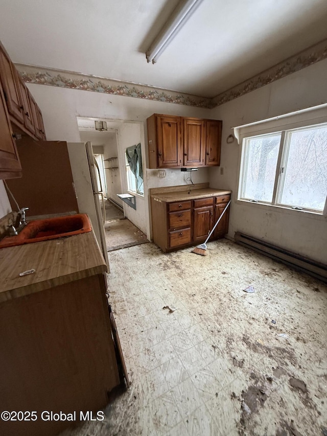 kitchen with a sink, light countertops, baseboard heating, brown cabinets, and light floors