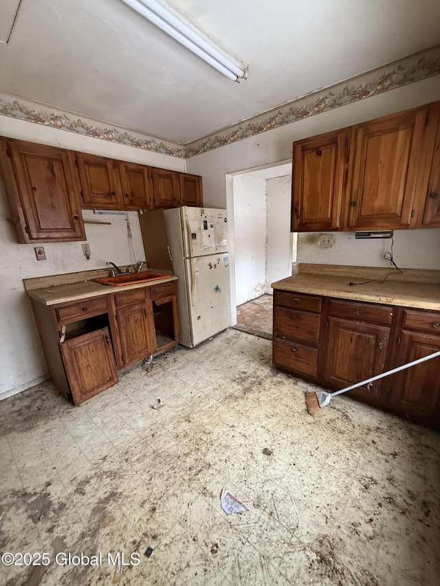 kitchen featuring light floors, light countertops, brown cabinetry, freestanding refrigerator, and a sink