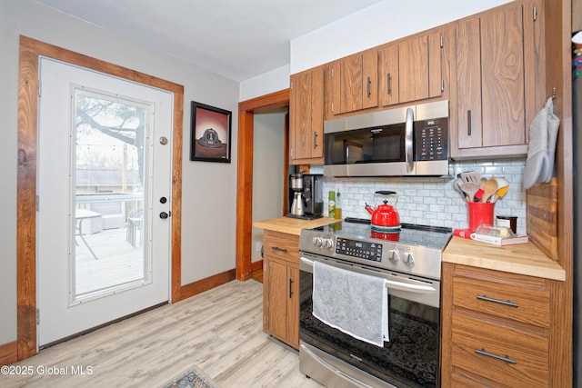 kitchen featuring light wood finished floors, appliances with stainless steel finishes, brown cabinets, and decorative backsplash