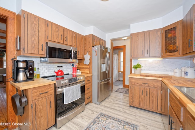 kitchen with tasteful backsplash, stainless steel appliances, butcher block countertops, and light wood-style floors